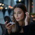 A compact mirror with LED lights, featuring a black exterior. A woman is using it in a softly lit urban setting.