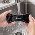 A black Sticky Nano Rubber Pad being washed under running water in a sink, held by two hands.