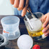 A whisky ice ball mould with a clear sphere of ice, tongs, and a drink in a glass, set on a wooden surface.