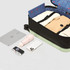 A collapsible suitcase in black and mint, with rolled clothing inside, alongside a tablet, camera, and smartphone.