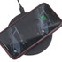 A black wireless charger with a smartphone placed on top, connected to a power source.