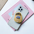 A yellow custom-shaped mirror phone pop holder on a clear phone case, resting on a pink book.