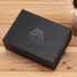 A black magnetic gift box with a textured finish and a logo on the top, placed on a wooden surface.