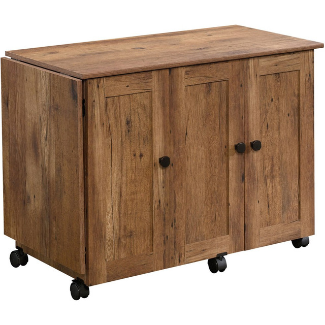 Take your crafting to the next level with help from the Sauder Select Sewing And Craft Table. A drop leaf table top offers additional workspace for bigger projects. Utilize adjustable shelves to organize all of your sewing and crafting accessories with ease.  Made from engineered wood.  Drop leaf workspace.  2 adjustable shelves.  2 storage bins.  1 hidden sewing machine shelf.  Roll-open door.  Easy-roll casters.  This product is heavy and/or oversized and may need more than one person to handle.