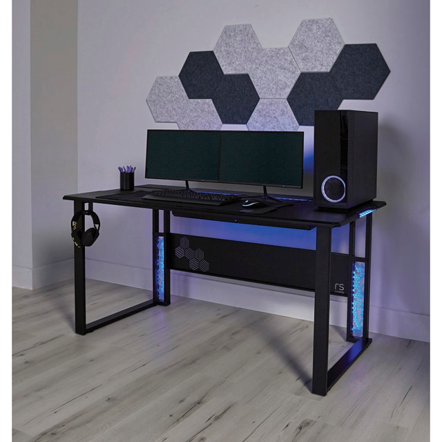 Bring your gaming experience to greater heights with the exceptional design of the RS Gaming Mergence gaming computer desk. The roomy carbon-fiber desktop of this Realspace desk gives you the space you need to set up your personal gaming preferences, while RGB lighting brings vitality to any scenario. The industrial desk features versatile cable management options, a USB hub, a headphone hook and other extras to add to your overall satisfaction.  60in wide carbon-fiber surface has a weight capacity of 176 lb (80 kg).  Includes a 3-port USB 2.0 hub, and concealed, under-desk cable trays plus a full-length, rear-hinged compartment for outstanding cord management options.  Remote-controlled RGB lighting on the desktop and legs has adjusting dynamic modes & speeds, color switching and adjustable brightness.  Improve your sound experience with the included 10-piece hexagon acoustic panels (self-adhesive & wall mountable).  Removable 38in x 13-1/2in (80 x 30 cm) mouse pad offers smooth, wide desktop coverage.  Includes convenient headphone hook, cable straps and 4 leveling glides.  Tested to meet ANSI/BIFMA Performance Standards - Manufacturer testing has been conducted on this product to meet specific performance requirements and safety standards set forth by the American National Standards Institute (ANSI) and the Business and Institutional Furniture Manufacturers.  This product is heavy and/or oversized and may need more than one person to handle.