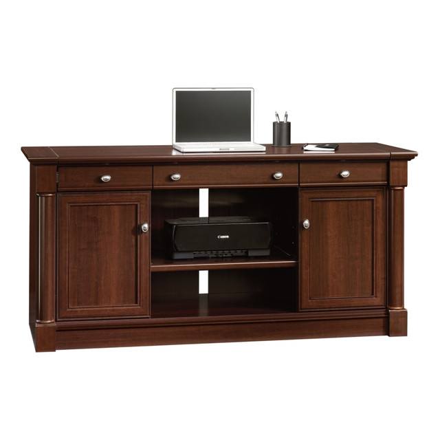 Find room for all your equipment without compromising workspace with this Sauder Palladia Computer Credenza. Charge your phone, laptop and tablet inside the hidden storage area underneath the top, and use the pull-out shelf at the center for your office printer. The hidden storage areas behind each door have adjustable shelves, so you can place extra paper, manuals and other necessities nearby.  Crafted with engineered wood.  Full-length cord pass-through.  Slide-out top and faux drawers with full-extension ball bearing slides reveal compartmentalized cord management and storage.  Computer desk with storage offers cupboards with adjustable shelves.  Pull-out, adjustable center shelf for equipment.  Assembly required.  Sauder cherry desk is handsomely finished.  This product is heavy and/or oversized and may need more than one person to handle.