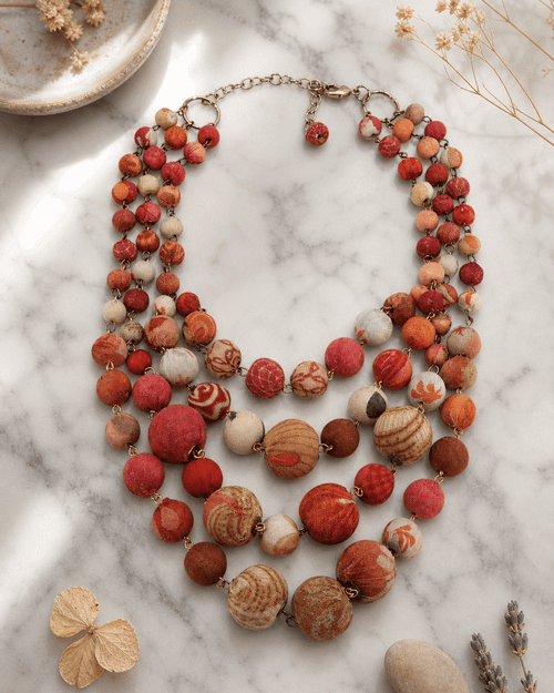 Layered kantha necklace in sunset orange and pink tones displayed on white marble surface