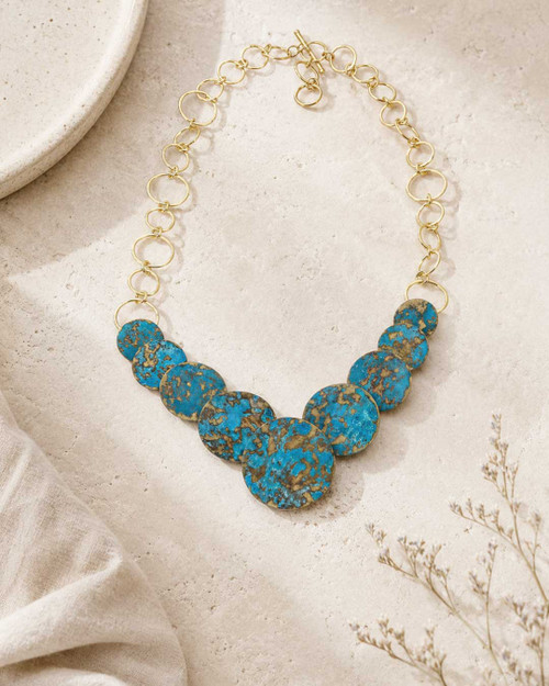 Hand-forged brass statement necklace with blue patina discs, front angle showing full length chain and pendant arrangement