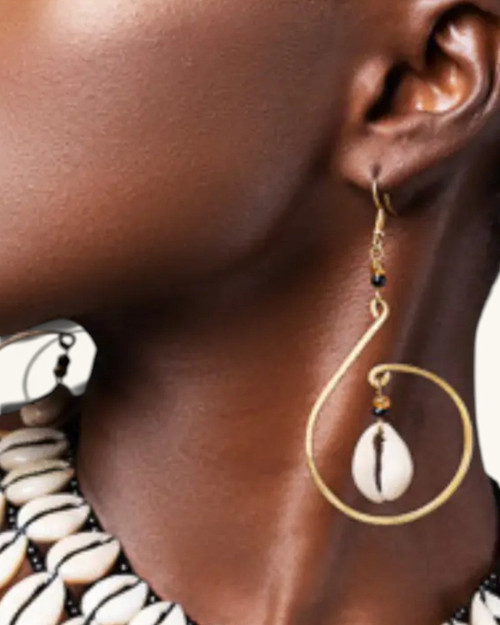 Cowrie shell hammered brass hoop earring worn on model's ear, side profile view showing full drop length and black bead detail