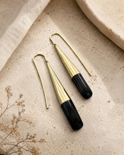 Tosha brass horn threader earrings flat-lay on stone surface, gold fluted cone with black horn drop detail
