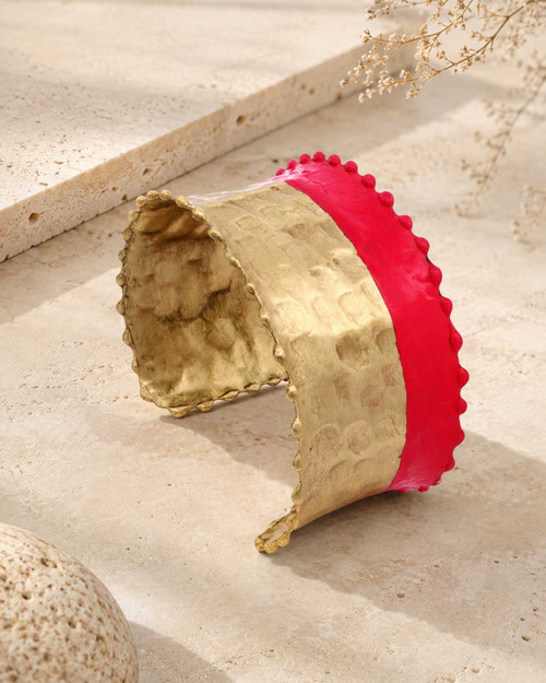 Hand-hammered brass cuff bracelet with red painted band displayed upright on stone surface with dried botanicals in background