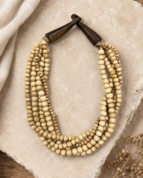 Five-strand bone bead necklace laid on a stone surface with dried flowers and draped linen fabric, styled flat lay