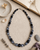 Hand-Painted Black Ceramic Pottery Bead Necklace with Metal Accents — necklaces, flatlay linen lifestyle photo