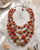Layered kantha necklace in sunset orange and pink tones displayed on white marble surface