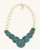 Hand-forged brass statement necklace with blue patina discs, angled front view showing chain texture and forged brass detailing