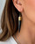 Kami black horn brass spike drop earring worn in ear, close-up profile view showing gold cylindrical cap and long tapered spike