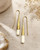 Tosha bone and brass threader drop earrings laid flat on stone surface with dried flowers and crystal props