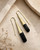 Tosha brass horn threader earrings flat-lay on stone surface, gold fluted cone with black horn drop detail