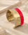 Hand-hammered brass cuff bracelet with red painted band displayed upright on stone surface with dried botanicals in background