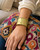 Beaded edge hand-hammered brass cuff bracelet worn on a wrist resting on a colorful woven pillow, worn view