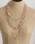 Three-strand mixed metal chain necklace draped on a tan dress form, showing gold, copper, and silver circle-link layers at the chest