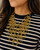 Brass ring bib necklace worn by a model over a navy and white striped sweater, showing full drape on the chest