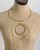 Brass collar necklace with nested double ring pendants displayed on a dress form, full front view