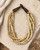 Five-strand bone bead necklace laid on a stone surface with dried flowers and draped linen fabric, styled flat lay