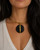 Horn and brass disc choker necklace worn by model, close-up showing black horn disc pendant with brass bar on gold collar