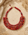 Red textile-wrapped bead layered bib necklace displayed on travertine surface