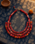 Red textile-wrapped beaded layered bib necklace on indigo fabric background with rim lighting