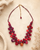 Kantha recycled textile layered bead necklace in red styled on a textured cream surface with dried botanicals alongside