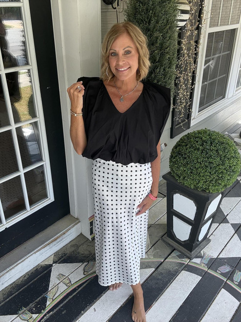 Woman posing in a black v-neck blouse and a satin white skirt with black polka-dots