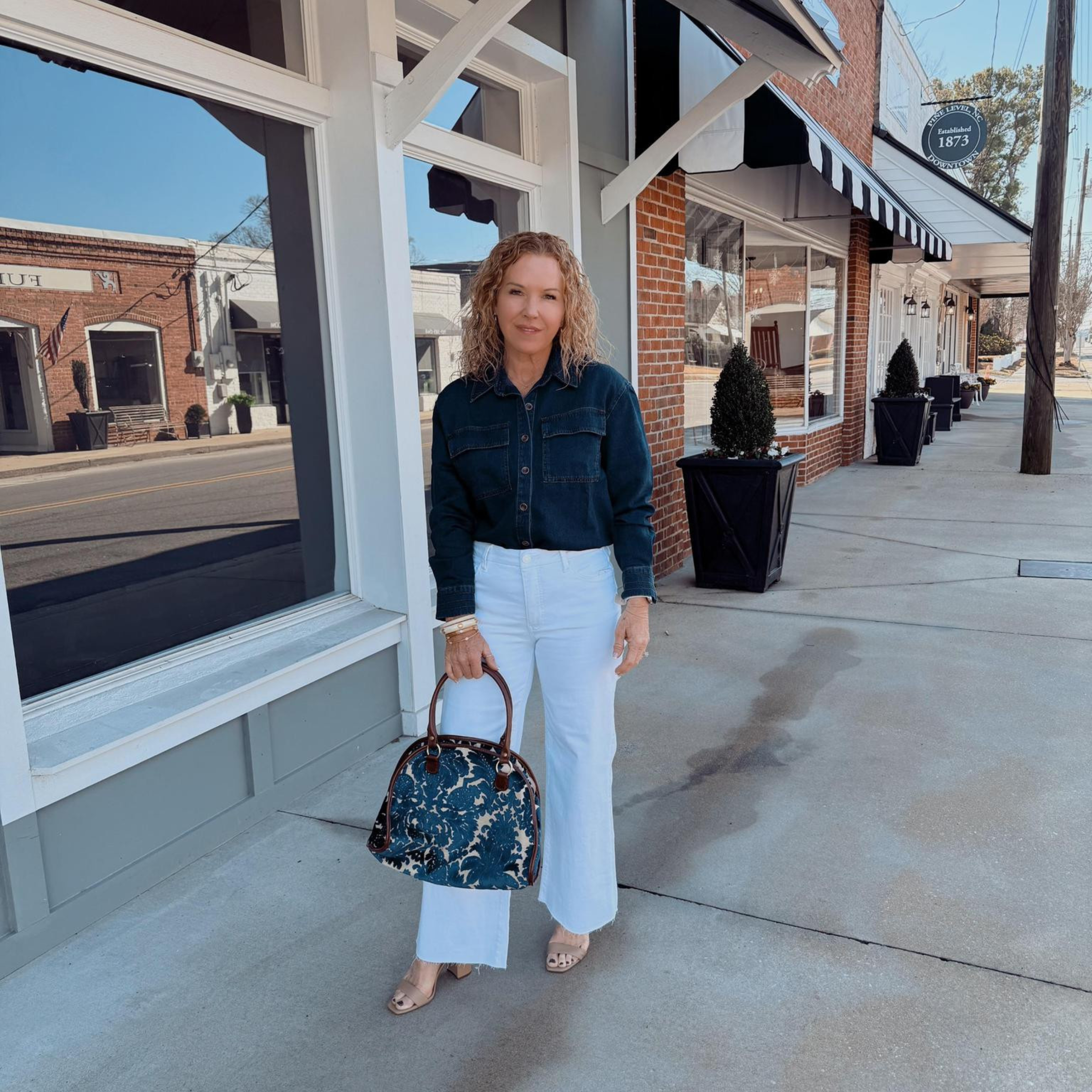 Woman's outfit including a dark denim button-up top and woman's white jeans