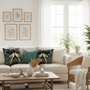 Warm living room detail with teal and gold crane decorative pillows on cream sofa, natural morning sunlight and plants
