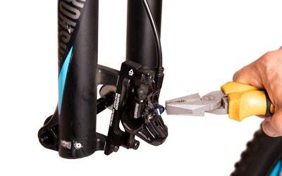 A close-up of pliers removing the retaining pin from a bike disc brake caliper
