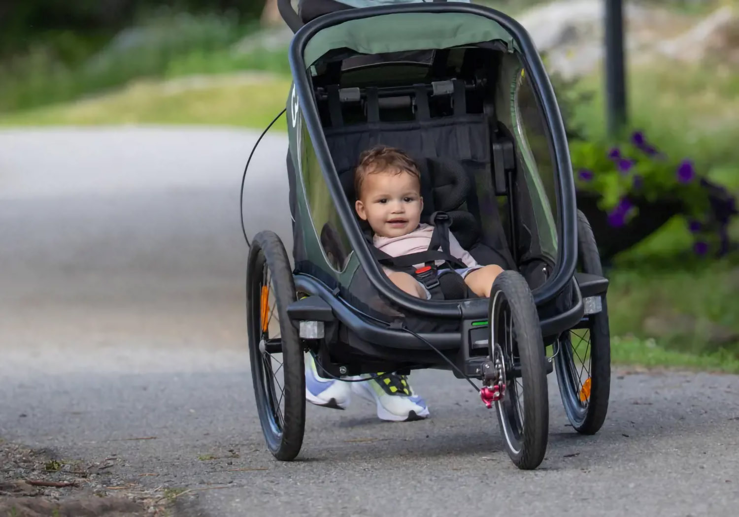 Hamax Outback 2-seat trailer with all-terrain jogger wheel on a bush trail with two children