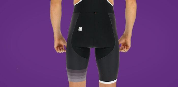 Back view of black cycling bib shorts with gradient-patterned side panels, displayed on a purple background