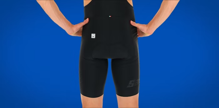 Close-up view of a cyclist wearing black bib shorts, showcasing the back panel design against a blue background