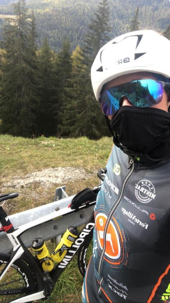 Cyclist in full gear with helmet, sunglasses, and winter face mask posing with a road bike