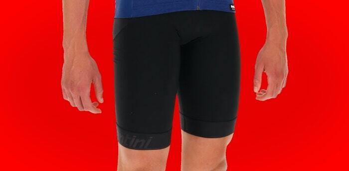 Cyclist wearing a blue jersey and black cycling shorts standing against a red background