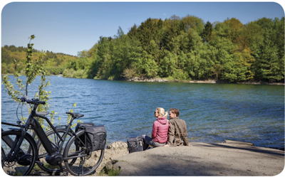 Cyclists relaxing near a river, with electric bikes parked beside them