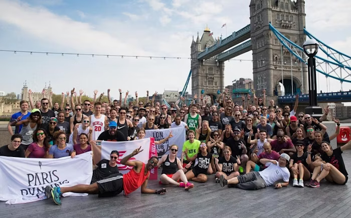 Large group of runners posing in front of Tower Bridge, some holding banners with city names, celebrating a running event.