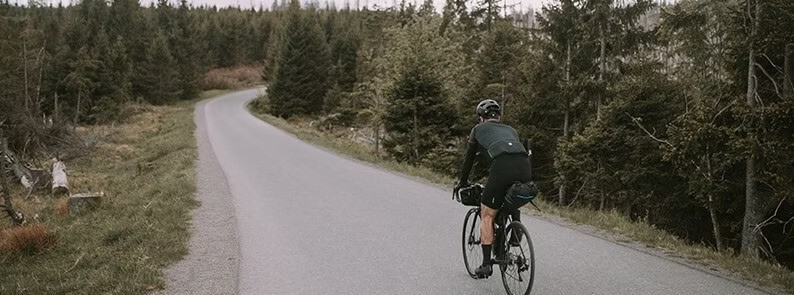 Cyclist riding on a winding forest road, surrounded by dense trees and a tranquil landscape.