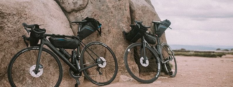 Two road bikes equipped with bikepacking bags leaning against large rocks in a rugged, open landscape.