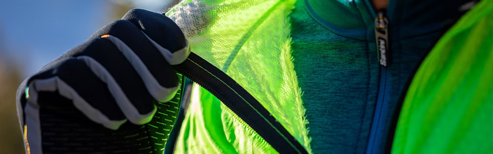 Close-up of a cyclist wearing gloves, adjusting a neon green jacket with a fleece lining.