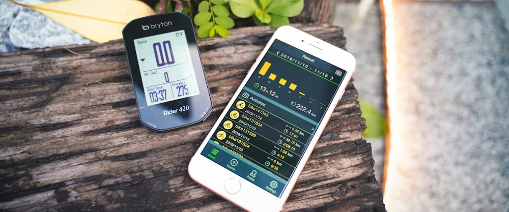 Bryton Rider 420 cycling computer and a smartphone displaying ride statistics on a wooden surface.