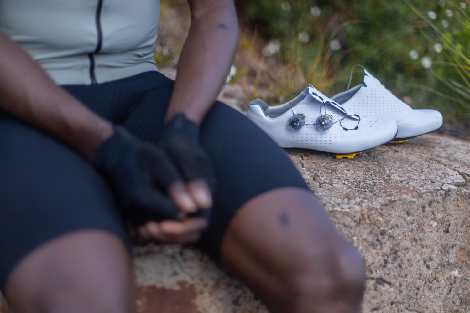 Cyclist sitting on a rock with white cycling shoes placed beside them.