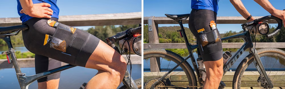 Cyclist leaning on a bridge railing, wearing cycling shorts with nutrition gels stored in the side pockets, next to a bike.