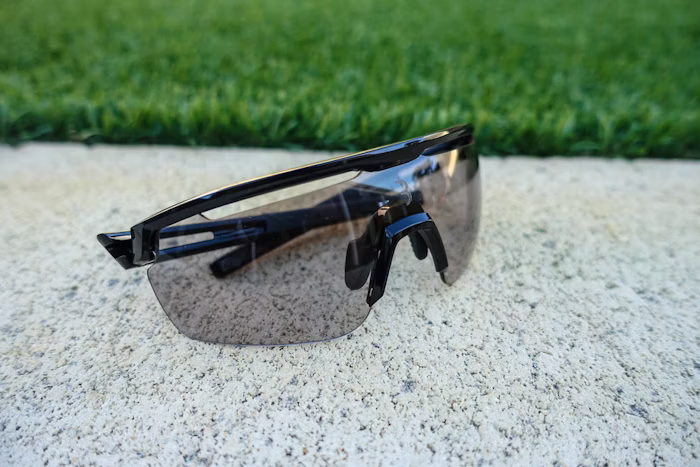 Black sports sunglasses with tinted lenses placed on a concrete surface, with grass in the background.